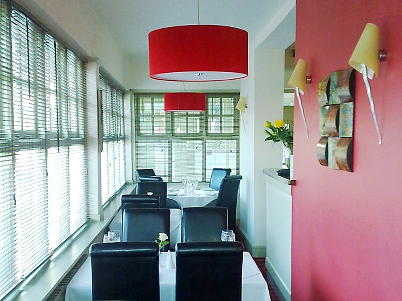 The conservatory dining area with red pendant shades, blinds and a pink feature wall